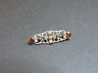 Lot 35 - A gold diamond and garnet scrolled bar brooch