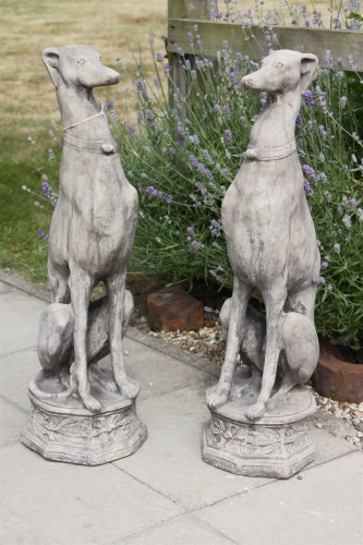 Lot 617 - A pair of cast stone garden sculptures of whippets seated on octagonal bases