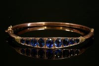 Lot 486 - An Edwardian 9ct gold graduated synthetic sapphire and garnet-topped doublet hinged bangle