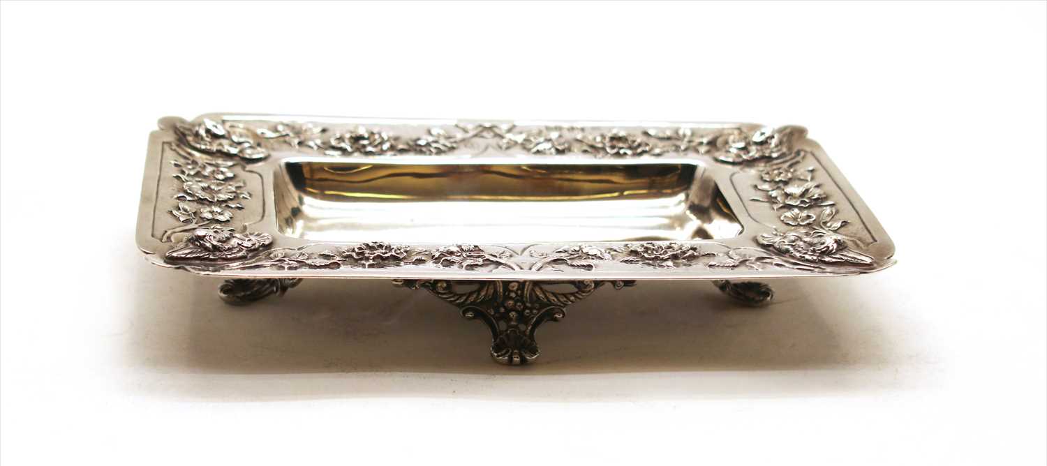 Lot 143 - A silver rectangular shallow dish having floral relief border and raised on shell form feet