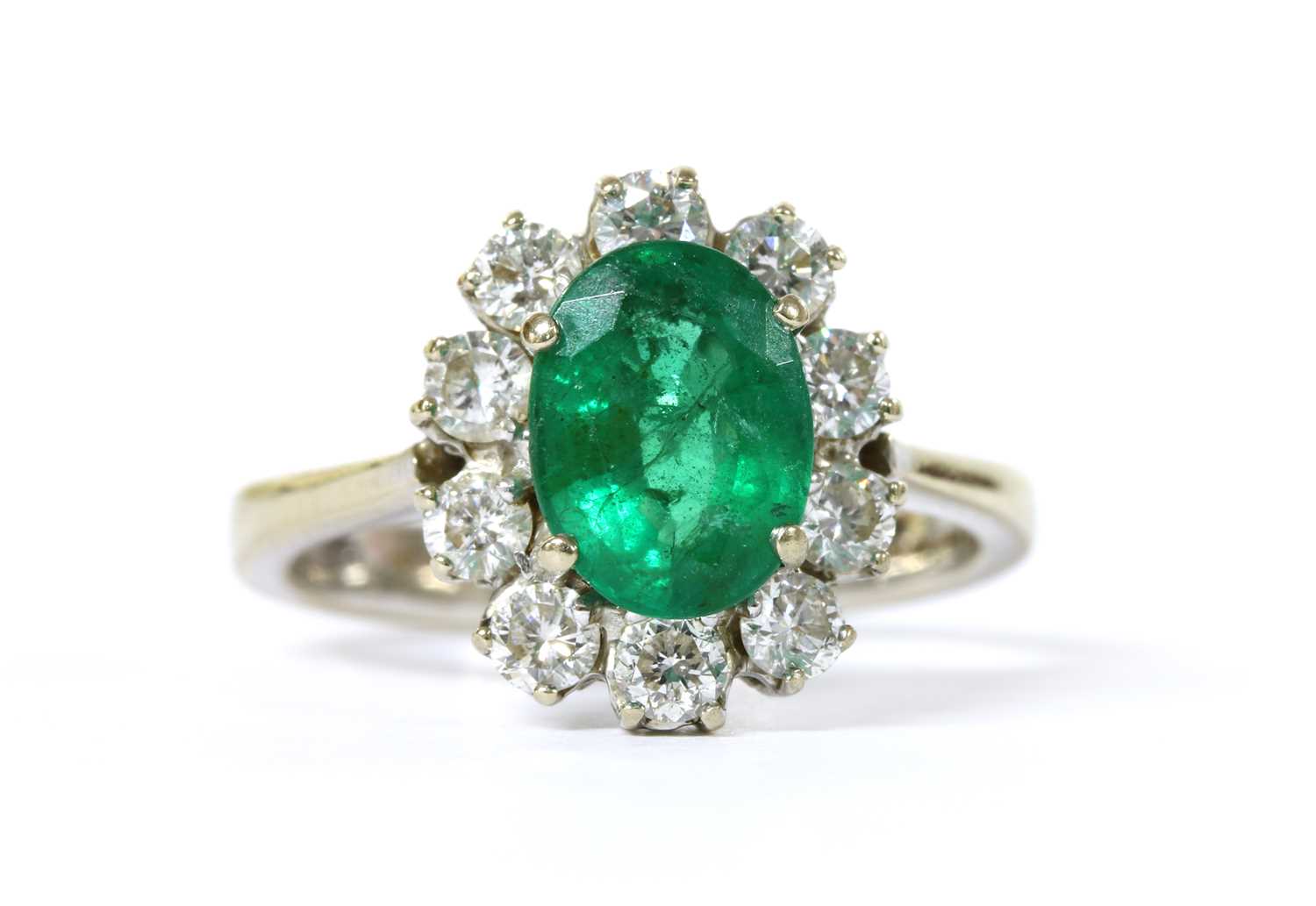 Lot 1187 - An 18ct white gold emerald and diamond oval cluster ring