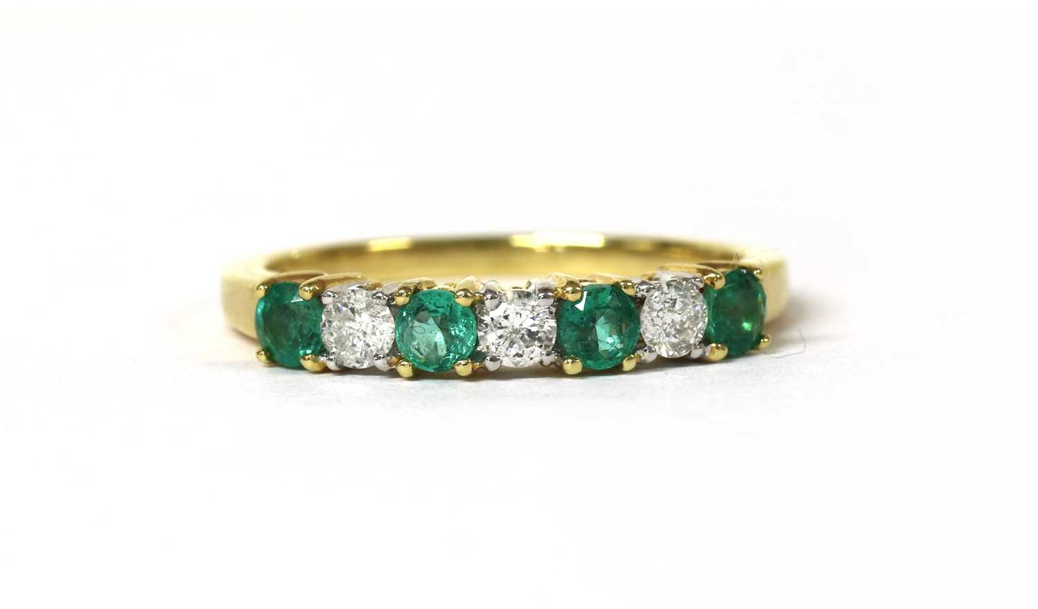 Lot 125 - An 18ct gold emerald and diamond half eternity ring