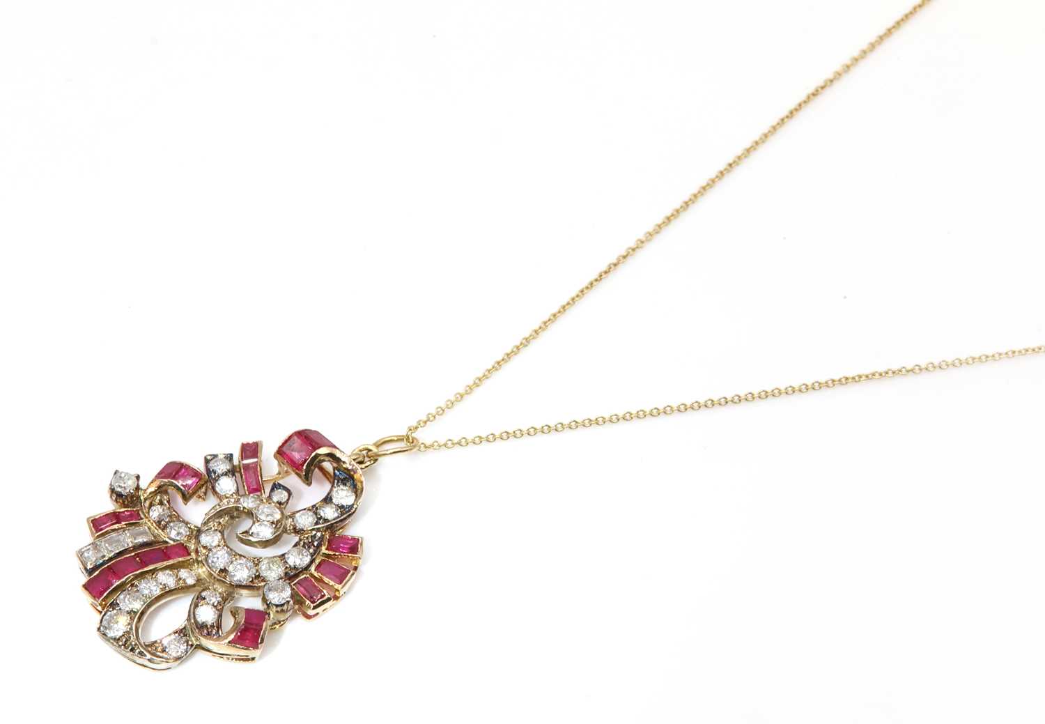 Lot 192 - A calibre ruby, synthetic ruby and diamond scroll pendant, c.1935