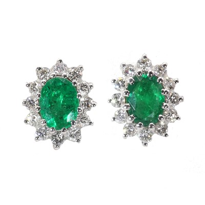 Lot 104 - A pair of white gold emerald and diamond oval cluster stud earrings