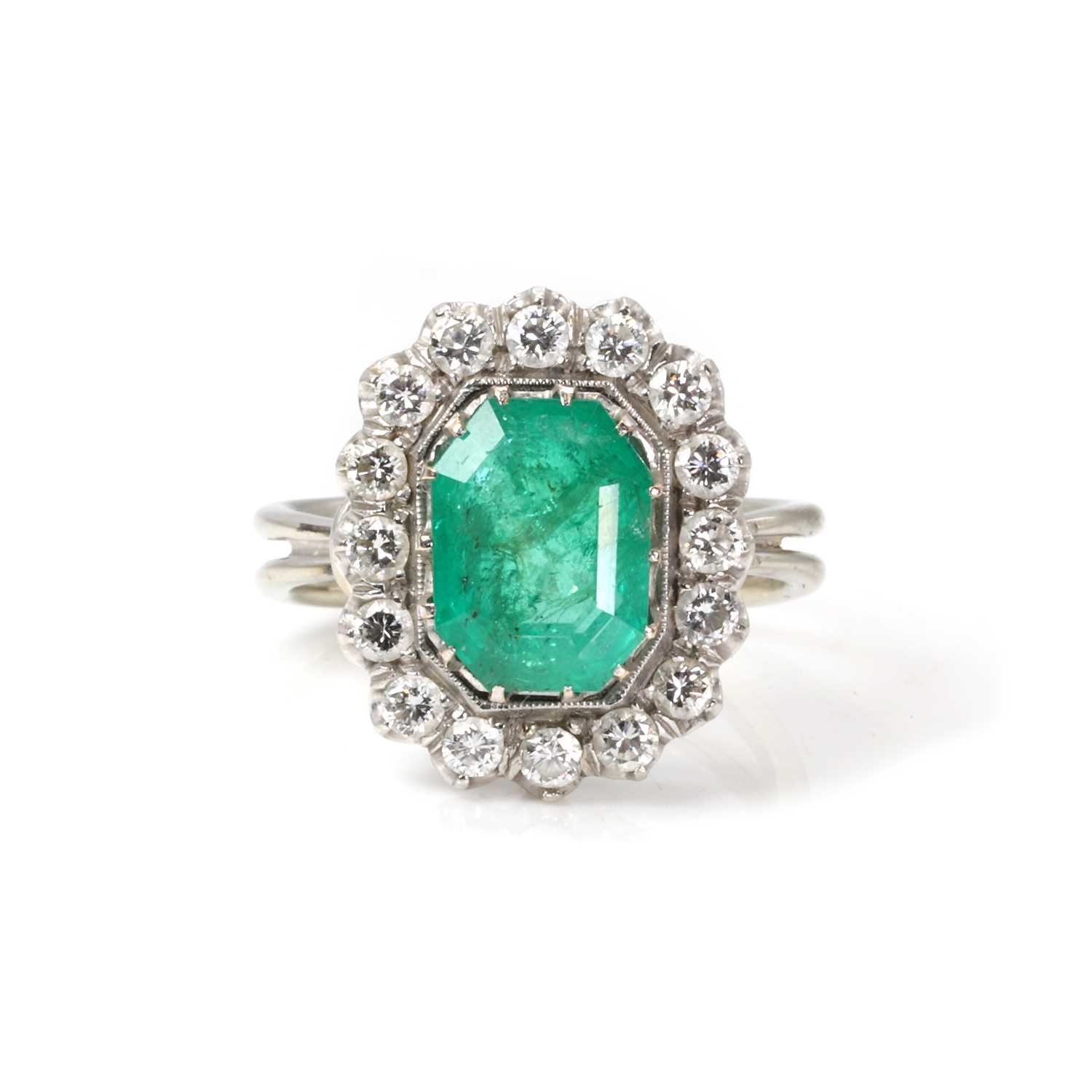 Lot 1183 - A white gold emerald and diamond cluster ring