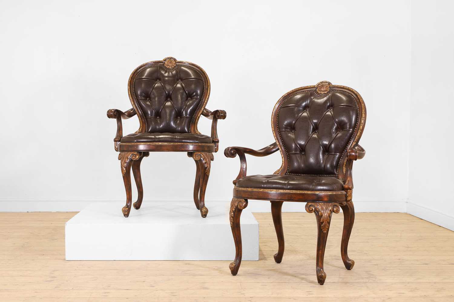 Lot 9 - A pair of buttoned leather and parcel-gilt wooden armchairs